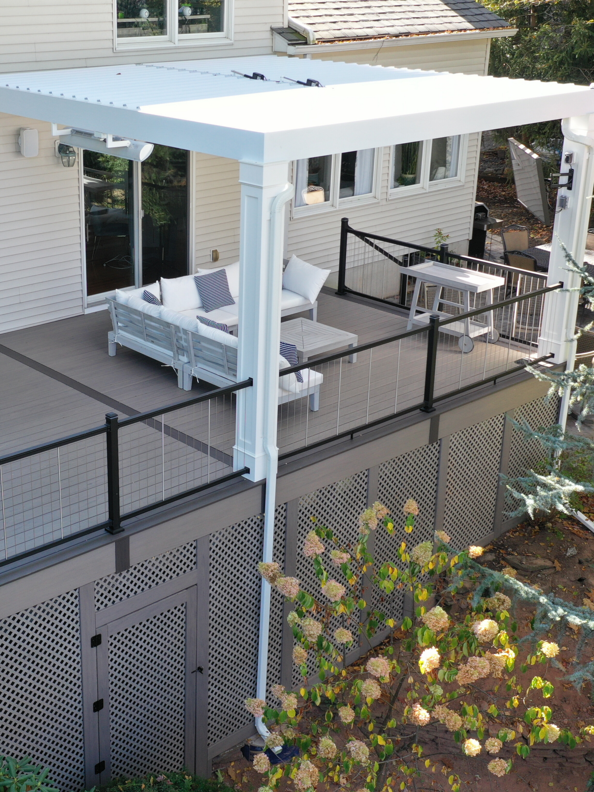 Deck in Westwood using composite decking and cable railings with a louvered pergola and lattice skirting